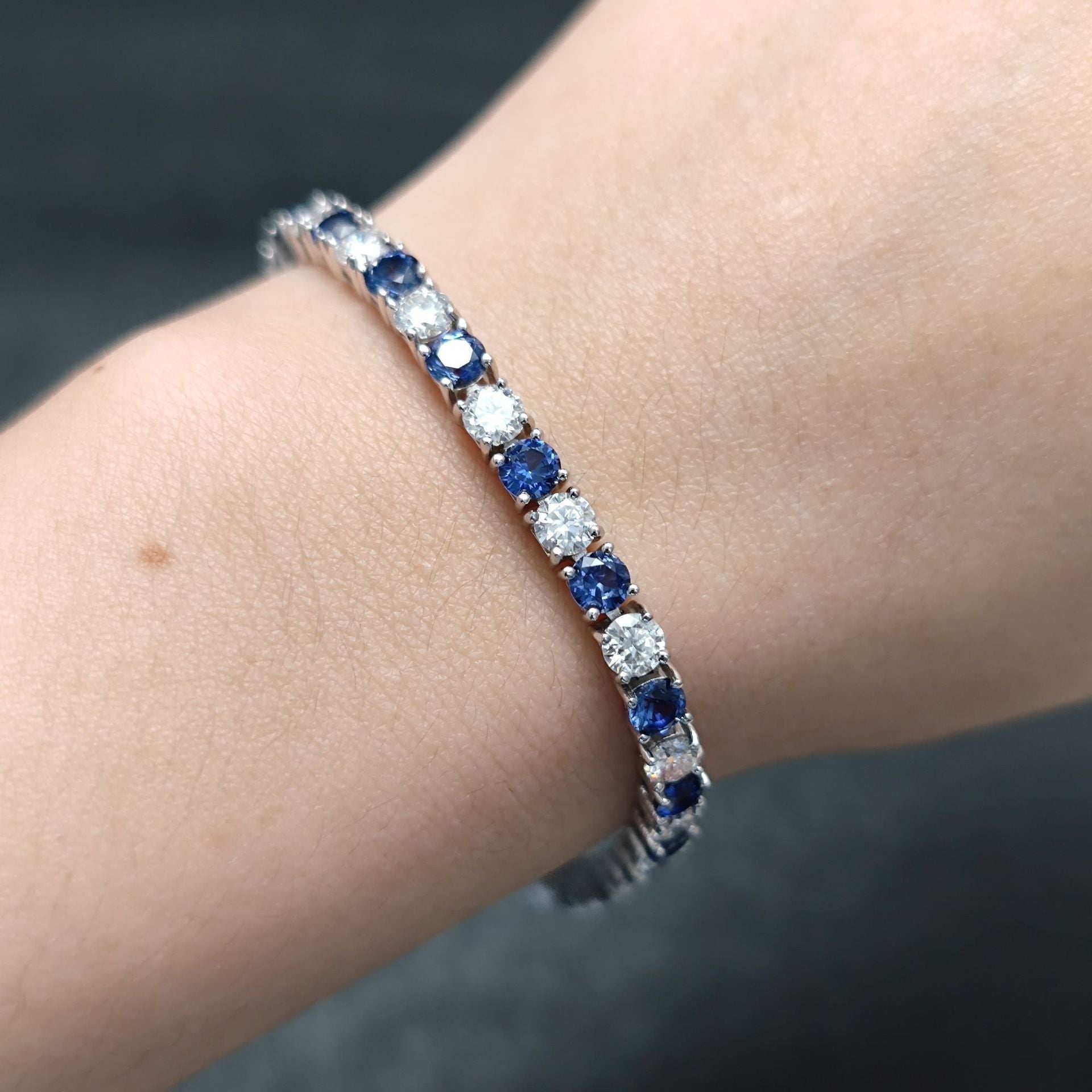The model showcases the synthetic sapphire mossanite tennis bracelet with rhodium plating.