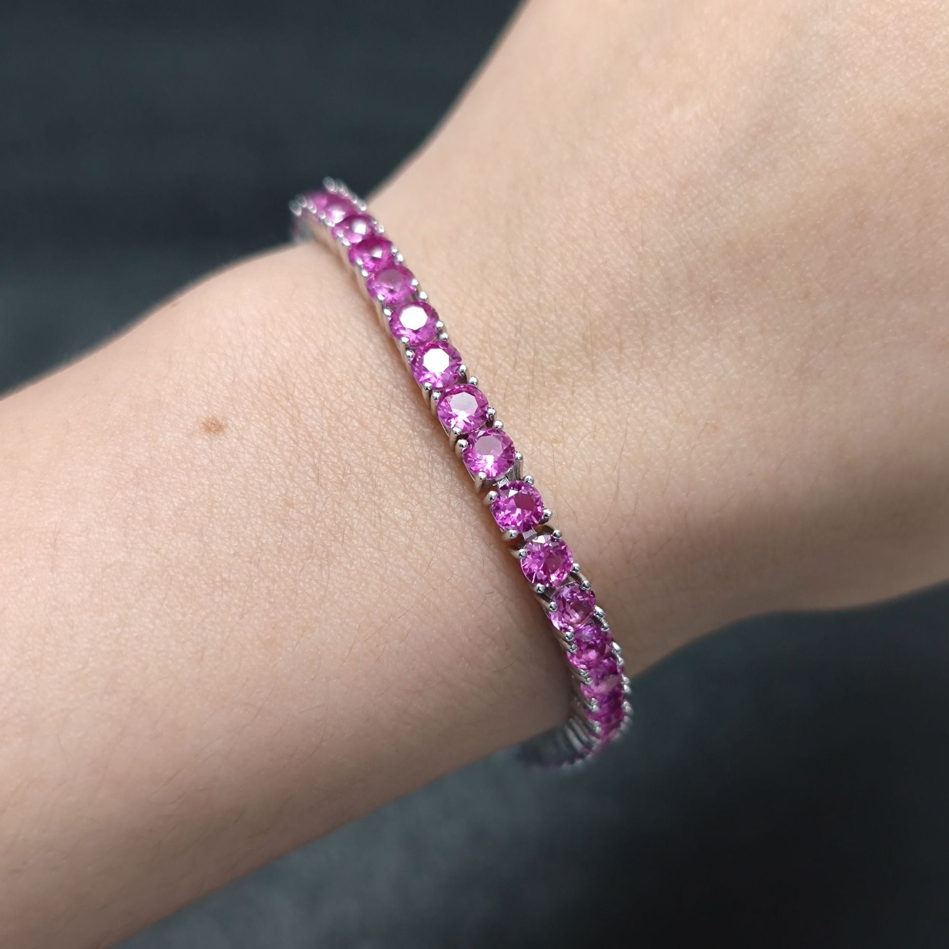 The model showcases the pink synthetic sapphire tennis bracelet. Plating with rhodium.